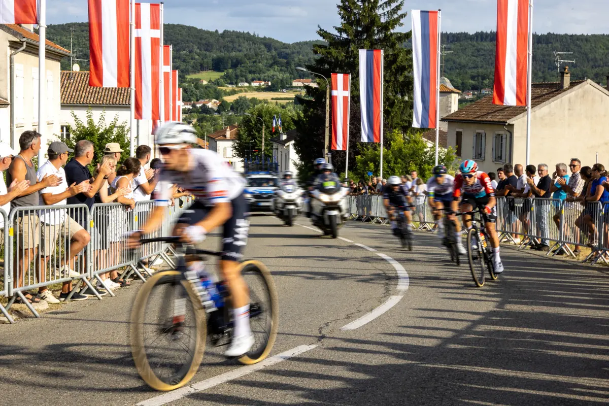 Cyclistes en course sur route sinueuse, bordées de spectateurs et de drapeaux rouges et blancs.