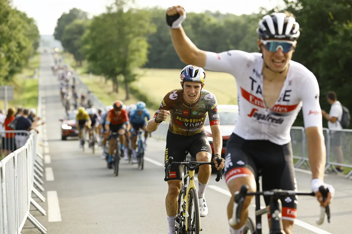 Cyclistes franchissant la ligne d'arrivée en célébrant, foule et voitures en arrière-plan rural.