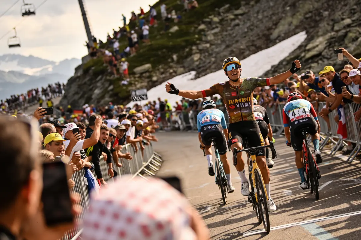 Cycliste levant les bras en victoire, entouré de spectateurs sur une route de montagne.