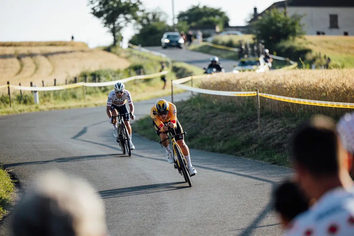 Deux cyclistes en compétition sur une route sinueuse, entourés de paysages champêtres et spectateurs flous.