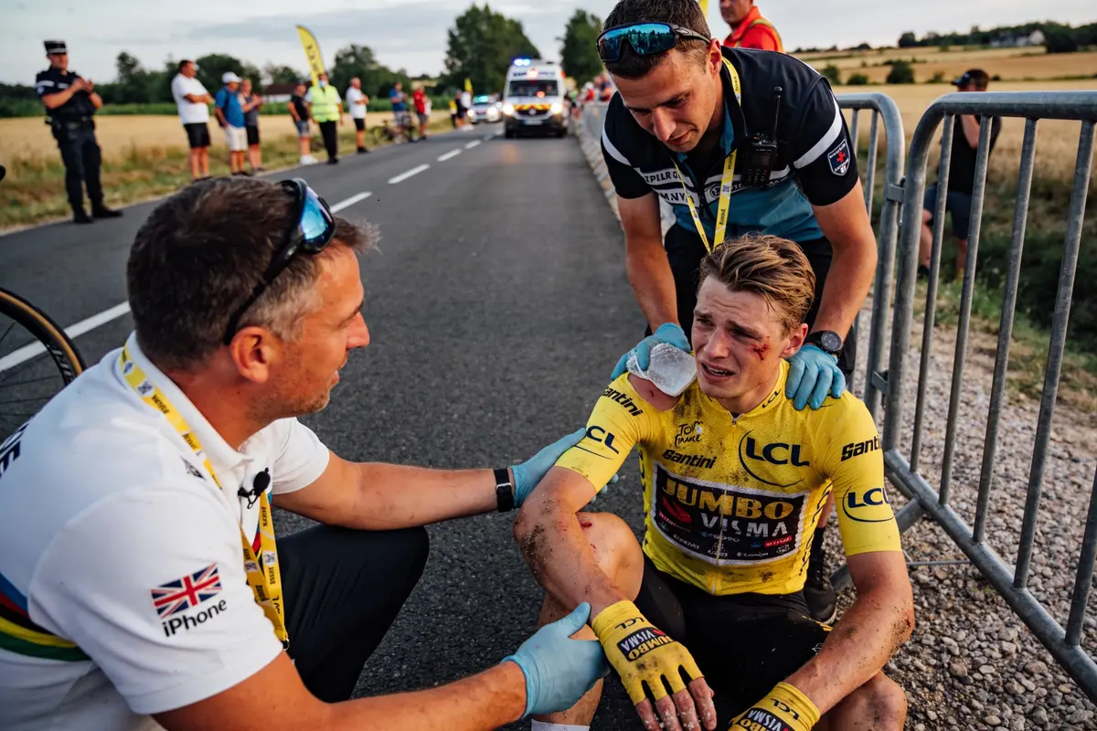 Cycliste blessé en jaune, entouré de deux secouristes sur une route, après une chute.