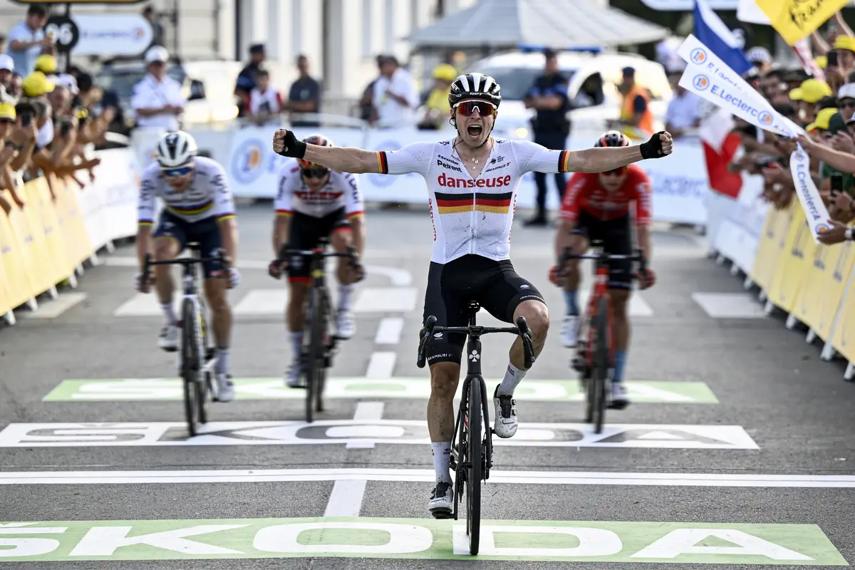 Cycliste franchissant la ligne d'arrivée, bras levés, en tête d'une course, suivi de concurrents.