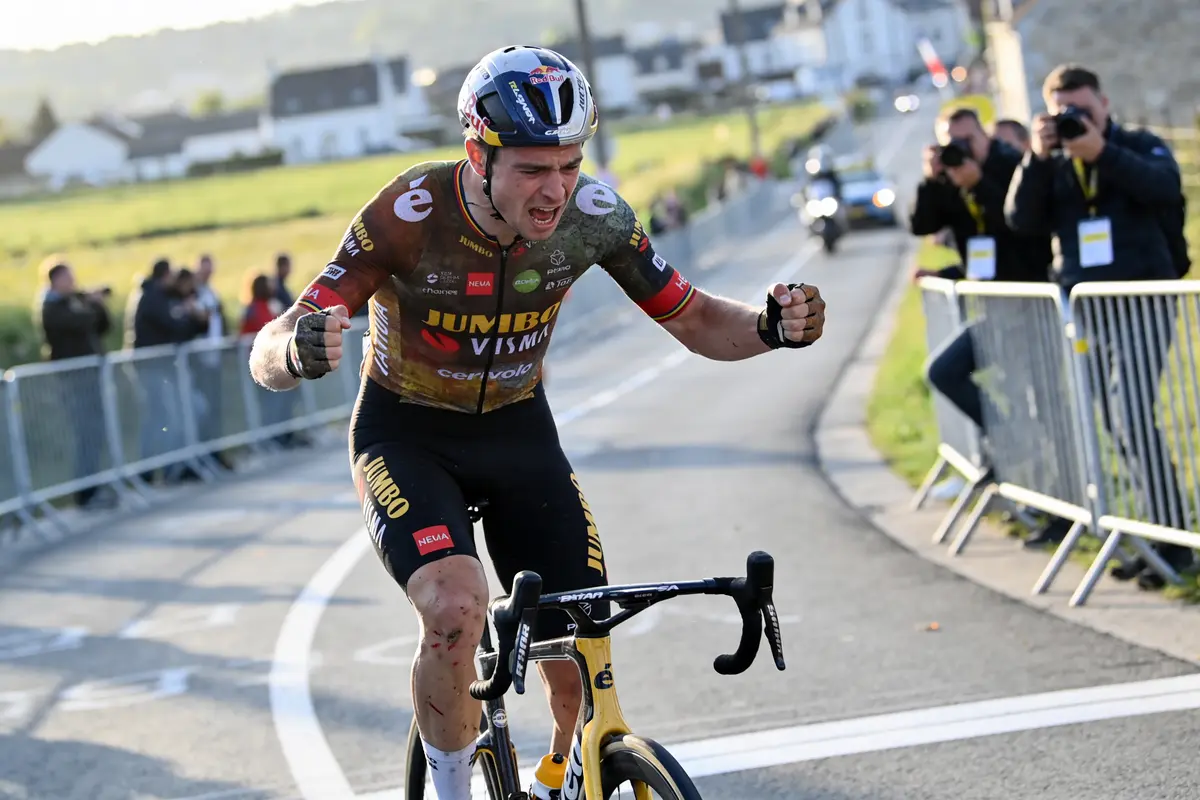 Cycliste célébrant une victoire sur route, avec spectateurs en arrière-plan et paysage rural.