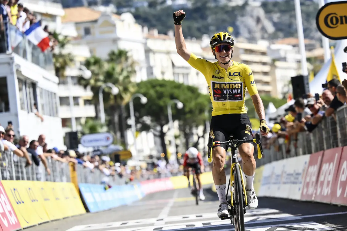 Coureur cycliste en jaune franchissant la ligne d'arrivée, public en arrière-plan agitant drapeaux français.