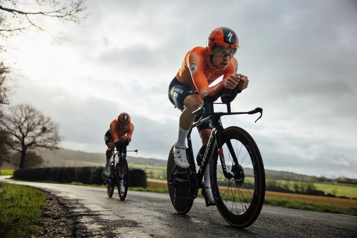 Deux cyclistes en tenue orange roulent sur une route de campagne sous un ciel nuageux.