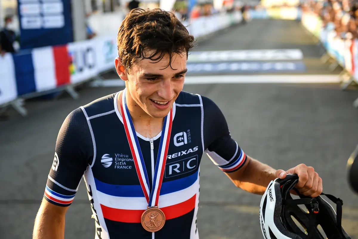 Cycliste souriant avec médaille de bronze et casque à la main, après une course.